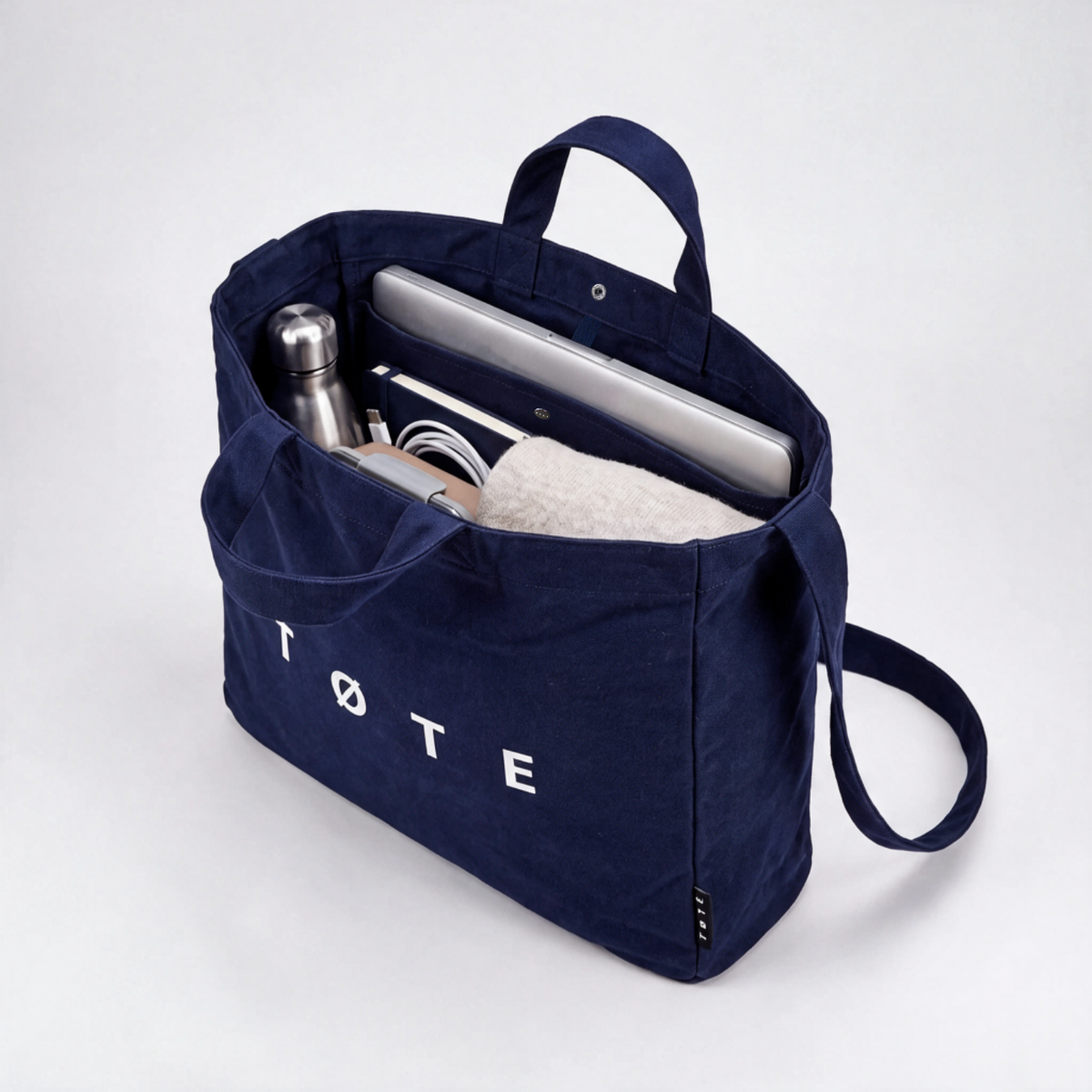 Navy Blue TØTE Bag packed with a laptop, water bottle, notebook, charger and a sweater