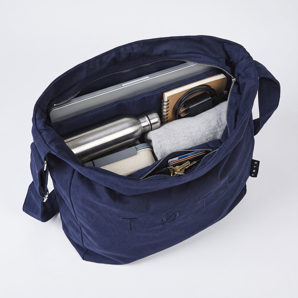A navy ALTA packed with a laptop, a notebook, a charger, a bottle, a lunch box, a jumper, cards and keys