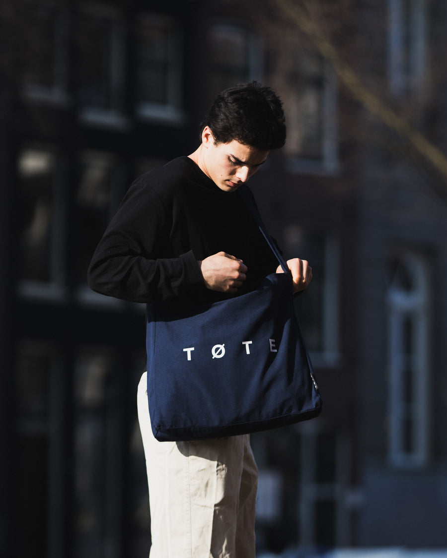 Reaching into the Navy Blue TØTE Bag beside a canal