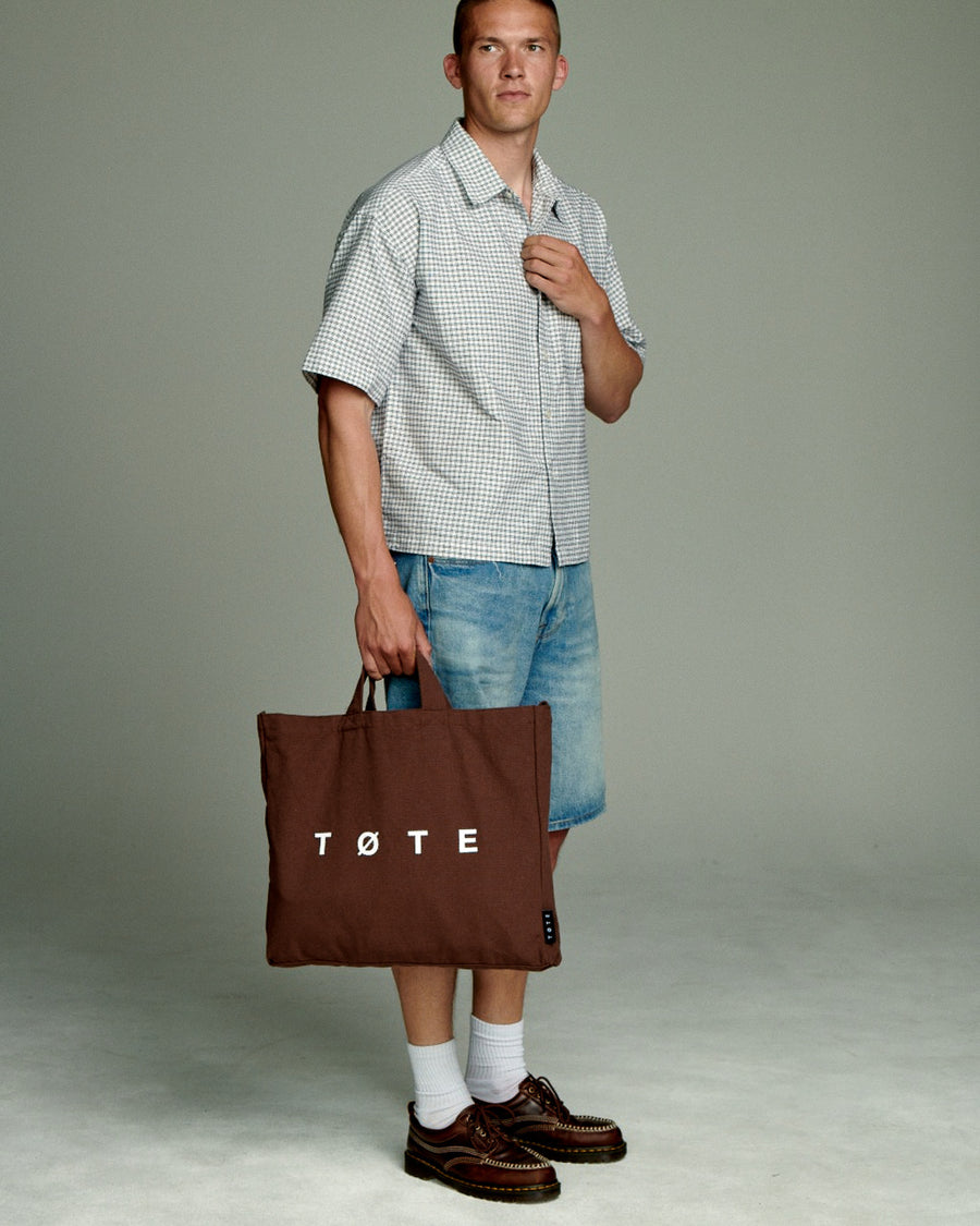 Brown TØTE Bag held by the handles against a studio backdrop